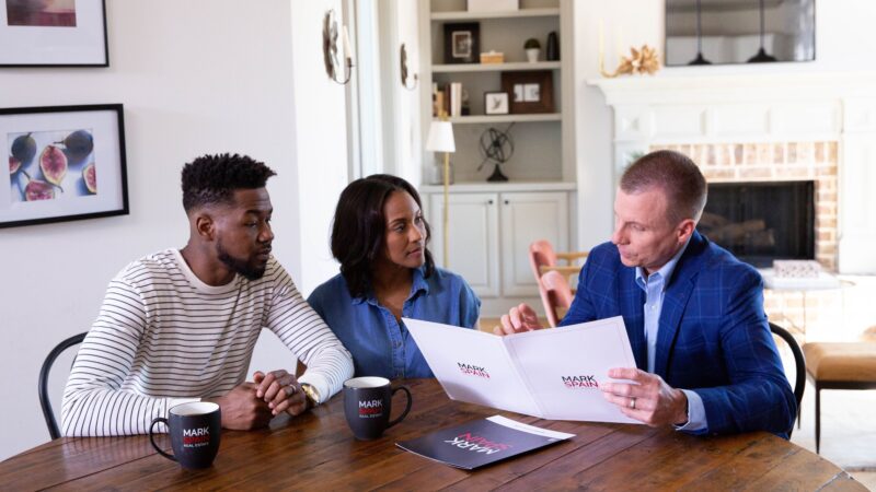 Mark Spain working with a couple at a table in a living room learning about what makes a good neighborhood to them.